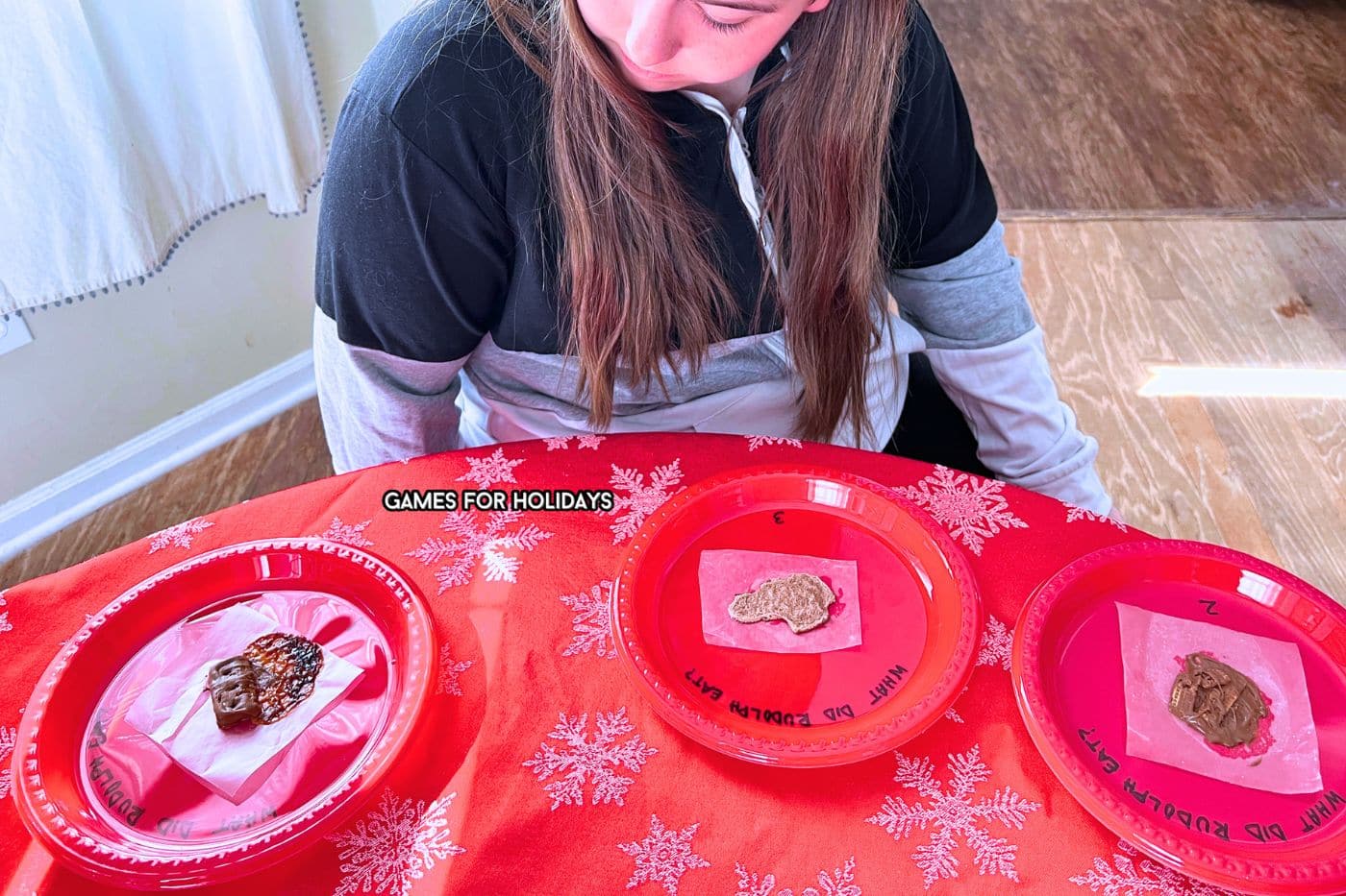 Christmas party guests looking at melted chocolates on plates on a Christmas table for the What Did Rudolph Eat The Reindeer Poo Game