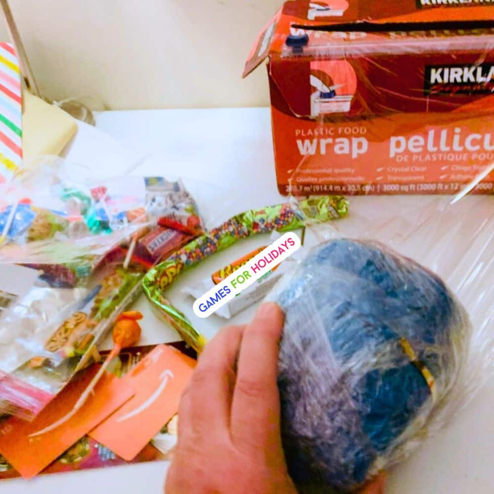 picture of how to wrap a Christmas ball plastic wrap game on a table with Christmas Saran Wrap game prizes